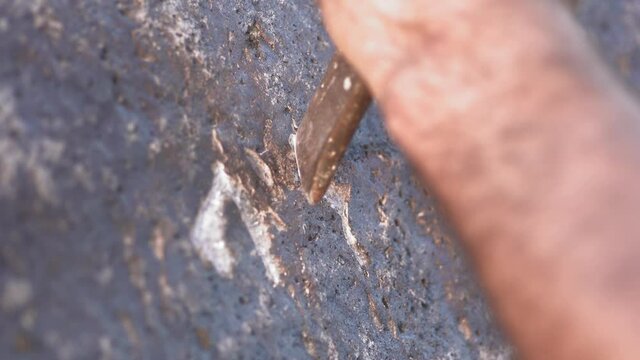 Prehistoric petroglyph carving reenactment using iron chisel on stone surface, close detail. Primitive rock inscription scene shows hand tools etching symbols into boulder, heritage craft footage.