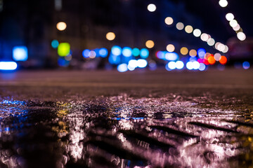Nights lights of the big city, the main city street in rushhour. Close up view of a puddle on the level of the hatch