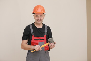 worker man in uniform, overalls and protective helmet is holding rubber hammer with yellow handle on white background
