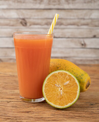 Orange and papaya juice in a glass with fruits over wooden table