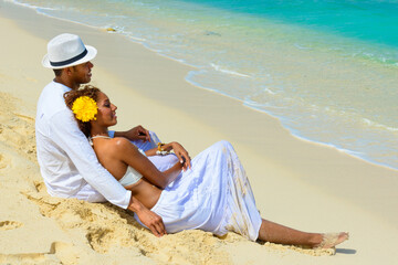 CCouple at the beach, on the seashore, close-up, interracial, black, dressed in white outfits, fun couples on the beach, sitting on the sand, woman reclining on the man 