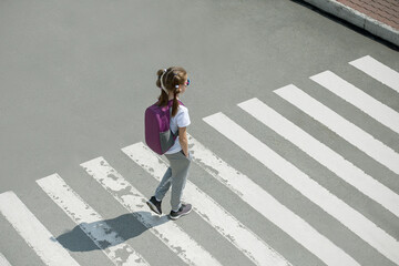 Schoolgirl crossing road on way to school. Zebra traffic walk way in the city. Concept pedestrians passing a crosswalk.  Stylish young teen girl walking with backpack. Active child.