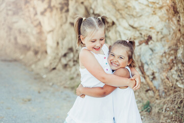 Two little sisters hug each other, smile and have fun outdoors near mountains