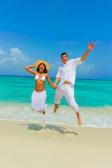 Girl and guy, couple at the beach, jumping on the seashore and waving, interracial, black, dressed in white outfits, fun couples on the beach