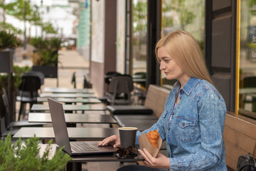 young woman sits at a table in a summer cafe with a laptop and drinks coffee