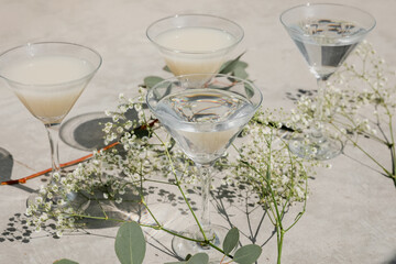 Summer drinks in martini cocktail glasses on warm grey concrete. Beautiful composition with gypsophila flowers and eucalyptus. Direct sunlight creating beautiful shadow.  