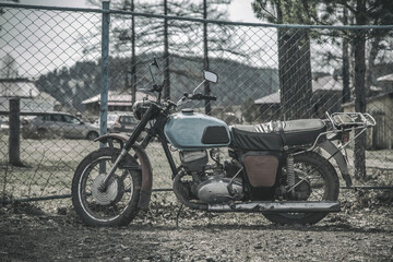 An old abandoned motorcycle stands by the fence. Beautiful nature. Abandoned old technology....
