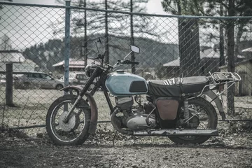 Foto op Plexiglas An old abandoned motorcycle stands by the fence. Beautiful nature. Abandoned old technology. Abandoned bike © Kooper