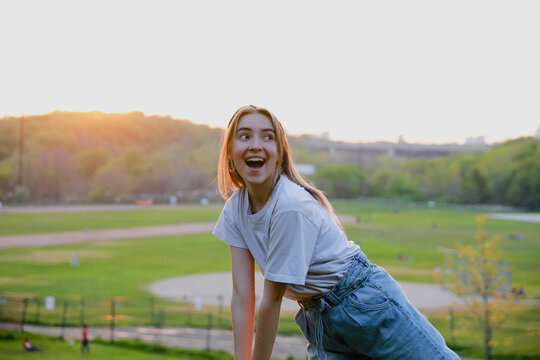 Happy young lady wearing jeans and a t-shirt looking to the side. Sunlit photo with beautiful sunset in the background. Summer happiness. 