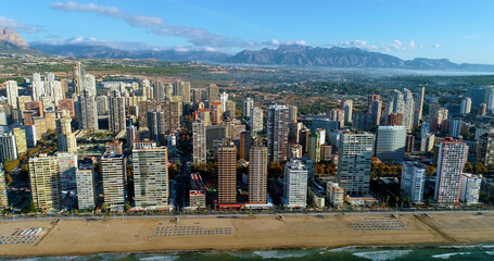 Benidorm city in Spain, with mountains in the background. We can see boats in the Mediterranean Sea and the buildings of the city near the shore - aerial view 4K