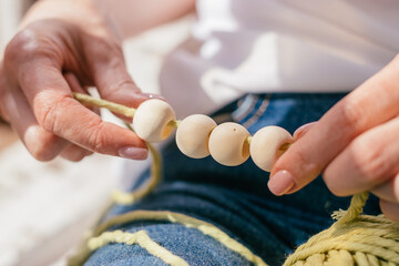 Close-up of a woman's hands stringing wooden beads on cotton thread for macrame.Handmade...