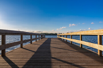 Fototapeta na wymiar Summer landscape with wooden jetty (pier) extend into the Nieuwe meer (New lake) is in southwest of Amsterdam, Beautiful blue sky with golden sunlight before the sunset, Amsterdamse Bos.