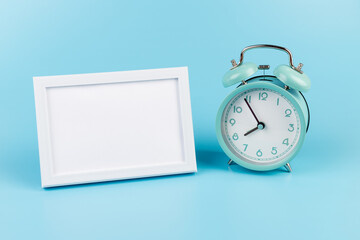 Photo frame and blue alarm clock on blue background with copy space.