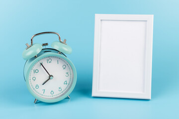 Photo frame and blue alarm clock on blue background with copy space.
