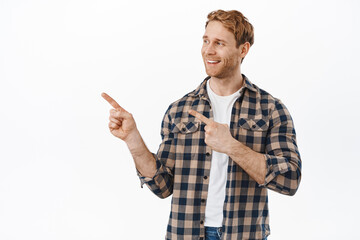 Handsome redhead man, ginger guy with bristle and blue eyes, looking confident and happy aside, pointing fingers left at good promo deal, nod in approval, satisfied with promotion, white background