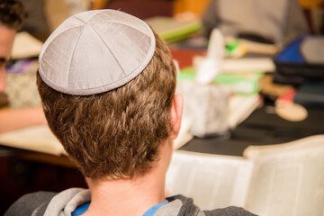 Young Jewish boy wearing yarmulke from the back typing on a keyboard at school. - obrazy, fototapety, plakaty