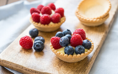 Homemade custard tartlets with raspberries and blueberries on the wooden table, close up