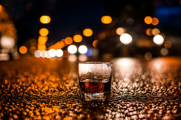 Lights of the city at night through the glass of alcohol, stream of cars traveling along the avenue. View from the glass level with brandy standing on the asphalt