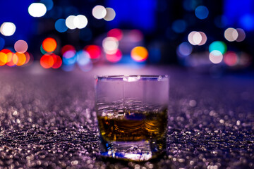 Lights of the city at night through the glass of alcohol, parking lights of the cars. View from the glass level with brandy standing on the asphalt