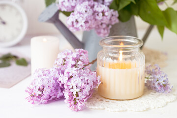 Fototapeta na wymiar Beautiful composition with fresh violet lilac bouquet in watering and candles. Cozy atmosphere. Greeting card for Saint Valentine's Day, 8 march, Women's day, Mother's day. White background