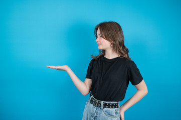 The teen girl in black t-shirt is holding something imaginary in her palm over blue background with empty space.