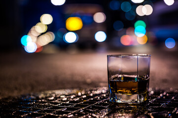 Lights of the city at night through the glass of alcohol, the night avenue with approaching bus. View from the glass level with brandy standing on the wet manhole