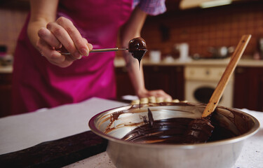 Chocolate pastry chef dipping pastry fork with candy into melted chocolate mass