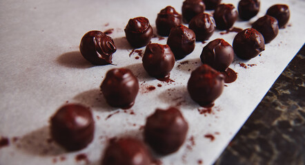 Beautiful chocolate truffles dipped in melted chocolate mass and sparkled with cocoa powder on a baking white paper on a marble table