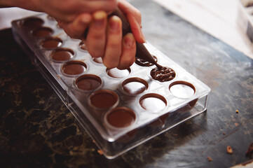 Pastry chef filling empty chocolate molds with filling for further preparation luxury homemade...