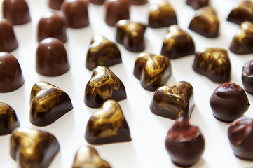 Assortment of beautiful luxurious Belgian chocolate candies, truffles and pralines with golden ornament in heart shape on a white background