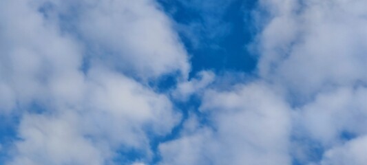 White and light gray clouds on the blue sky. On a clear sunny day, there are several high cumulus clouds against the backdrop of a clear, light blue sky. Clouds of different shapes and sizes.