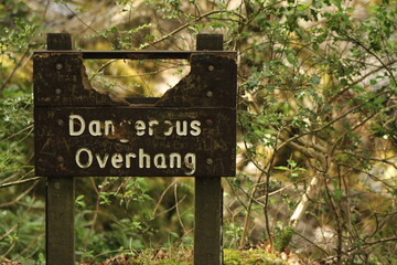 dangerous overhang sign close up with trees in background