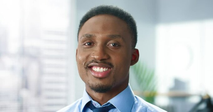 Close up of young happy handsome male office worker looking at camera and smiling. Positive emotions. African American cheerful businessman at workplace, cabinet, smile on face, business concept