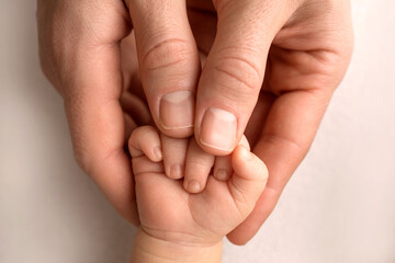 A newborn holds on to mom's, dad's finger. Hands of parents and baby close up. A child trusts and holds her tight