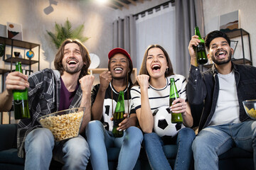 Excited young soccer fans supporting team during world cup champion while staying at home. Multi ethnic friends sitting on sofa with beer and snacks. Concept of people, sport and entertainment.