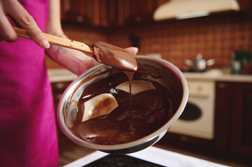 Pastry chef manufacturer of chocolate confectionery mixing melted chocolate mass in a steel bowl...