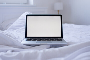 Blank laptop screen on a bed in a white bedroom.Mock up computer screen on white linen background.The laptop and computer in the morning on a white pillow bed. Lifestyle Concept.Work from home concept