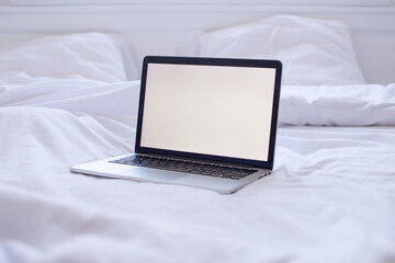 Blank laptop screen on a bed in a white bedroom.Mock up computer screen on white linen background.The laptop and computer in the morning on a white pillow bed. Lifestyle Concept.Work from home concept