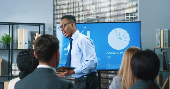 African American young handsome successful male business trainer speaking with employees making presentation to colleagues in office. Businessman presenting new development strategy project