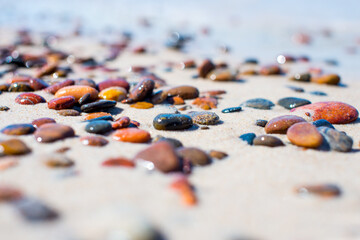 Colorful stones on the beach. The colorful stones lie on the sand and glisten in the sun. Depth of field. Background. Poster. Bokeh in the background. Copy space. 