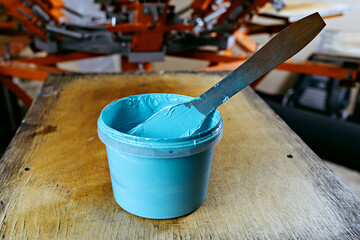 selective focus photo of can of blue paint on wooden shelve on the print screening apparatus. serigraphy production. printing images on t-shirts by silkscreen method in a design studio
