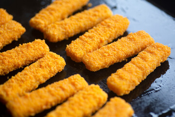 Fish sticks background. Fried fish sticks on a culinary baking sheet as an appetizer and food for children and parties.