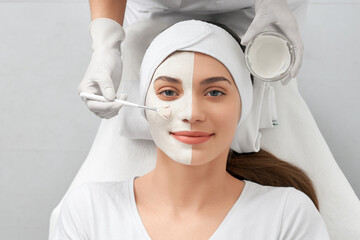 Front view portrait of beautician in white rubber gloves doing special beauty procedure for young smiling woman. Concept of improvements skin with cosmetics in beauty salon. 