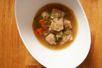 Top view of chicken and vegetable soup served in a white bowl on a wooden surface