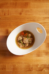 Top view of chicken and vegetable soup served in a white bowl on a wooden surface