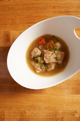 Top view of chicken and vegetable soup served in a white bowl on a wooden surface