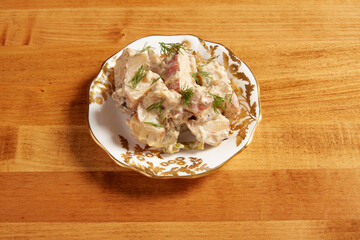 Potato salad served on a white plate with ornate gold details on a wooden surface