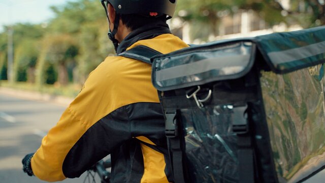 Food Delivery Man Wearing Protective Medical Face Mask and Thermal Backpack Rides a Bike to Deliver Order. Young Asian man working as a food delivery person. He riding a bike for sustainable way. - Powered by Adobe