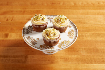 Carrot cake cupcakes served on a white cake stand with ornate gold details on a wooden surface