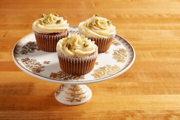 Carrot cake cupcakes served on a white cake stand with ornate gold details on a wooden surface